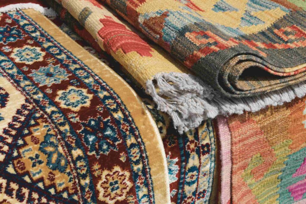  A collection of colorful rugs and carpets piled together, displaying an array of hues and designs.