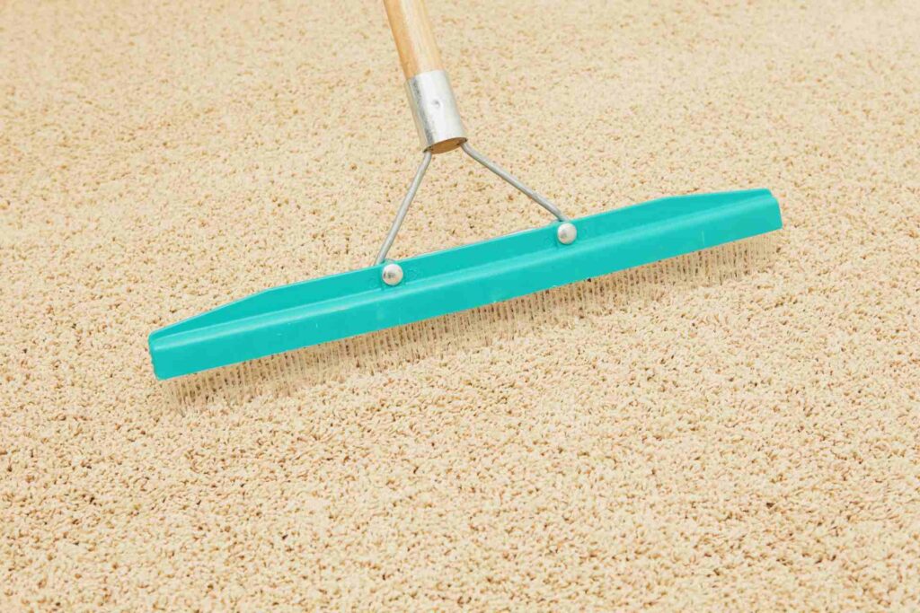 A person uses a green carpet rake to clean a carpet, effectively removing dirt and debris from the surface.