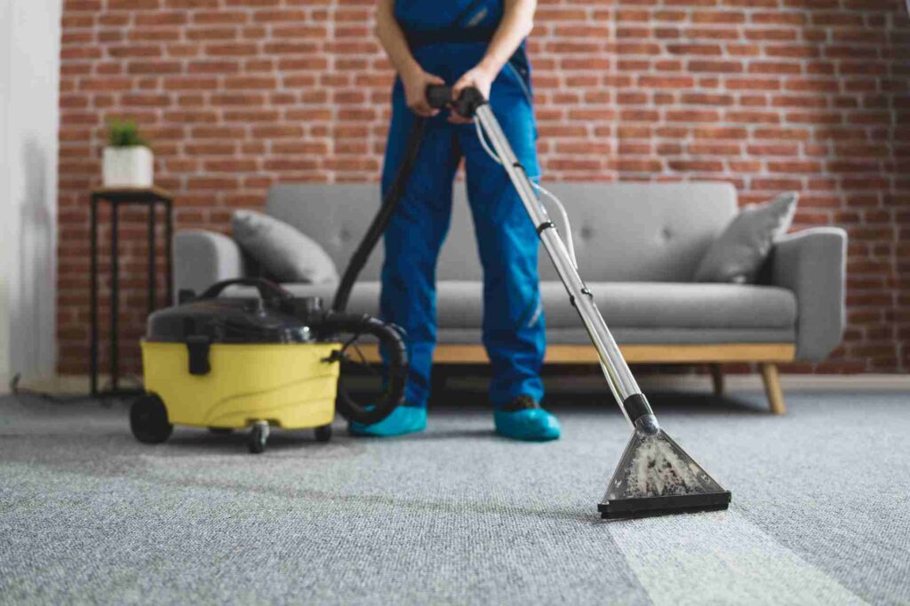 A man in blue overalls vacuums a carpet, ensuring a clean and tidy living space.