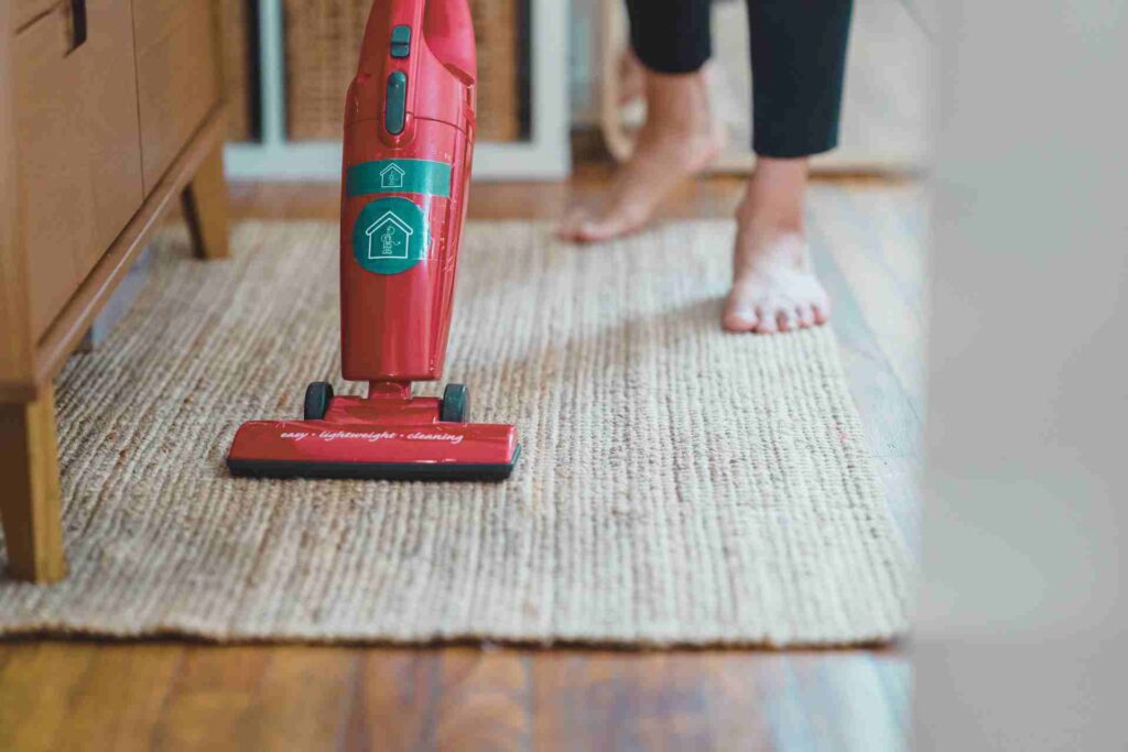 A woman vacuums a rug, demonstrating effective cleaning techniques in a well-lit room.