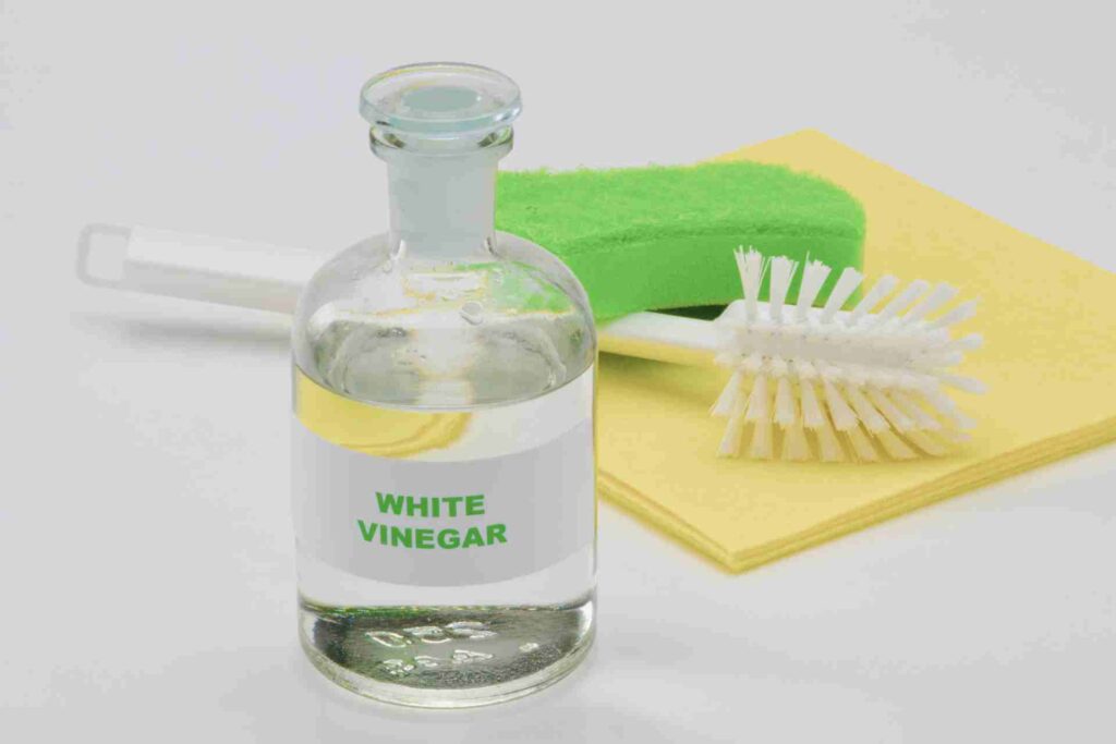 A bottle of white vinegar positioned beside a sponge and a cleaning cloth on a clean surface.